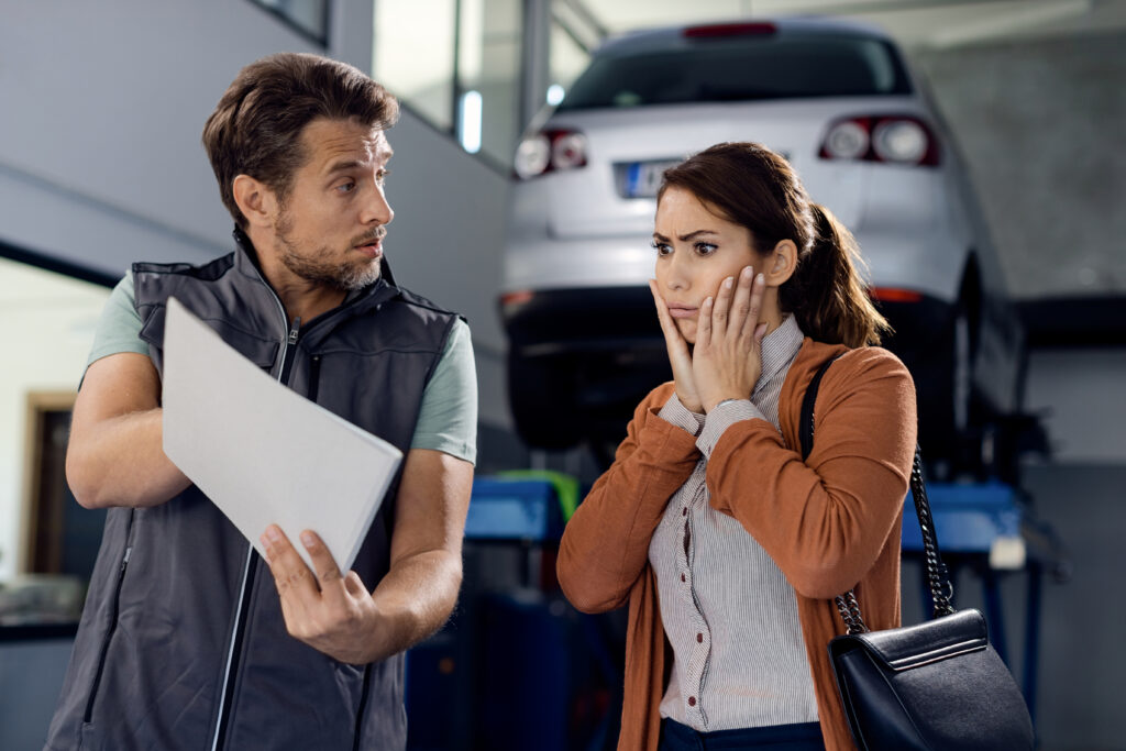 Auto mechanic showing report and car repair costs to shocked woman