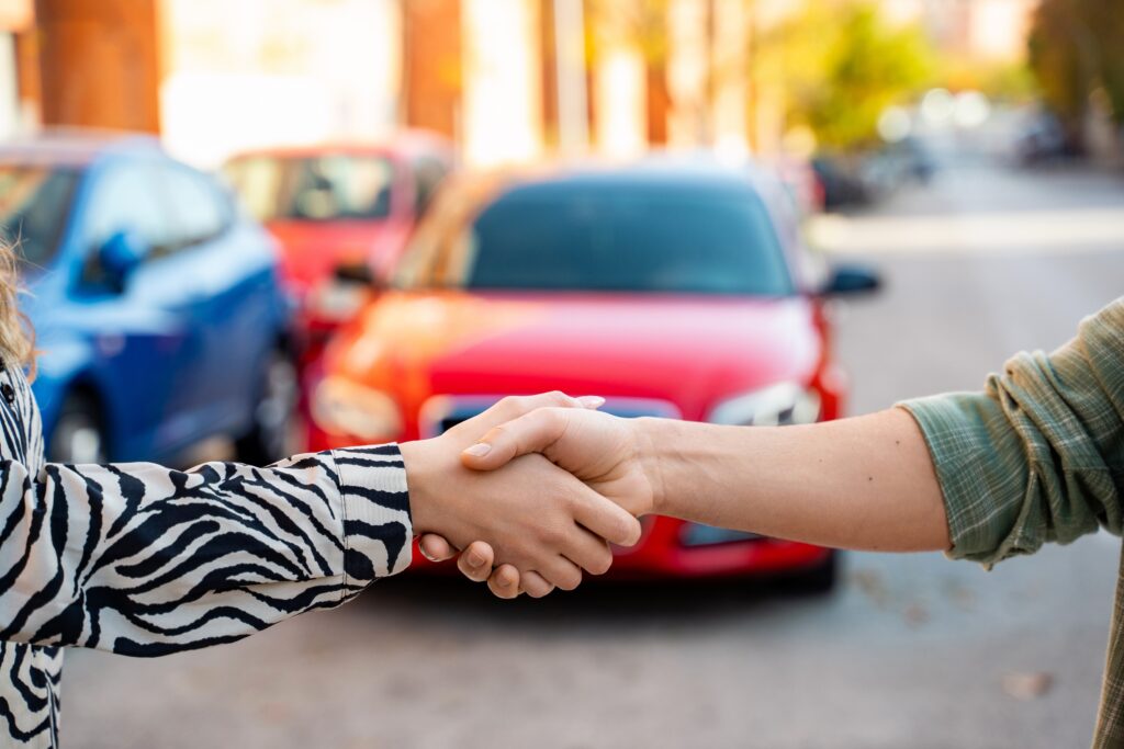 Salesperson shaking hands with customer in front of a red car