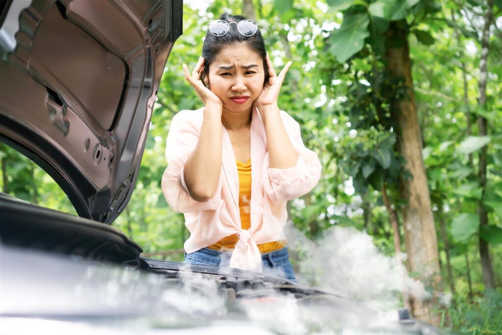 Woman looking under car hood to see smoke