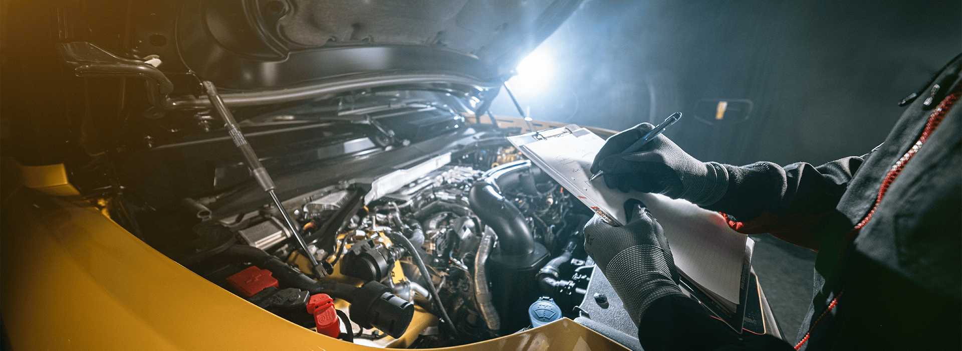 Mechanic inspecting car engine and writing notes on clipboard