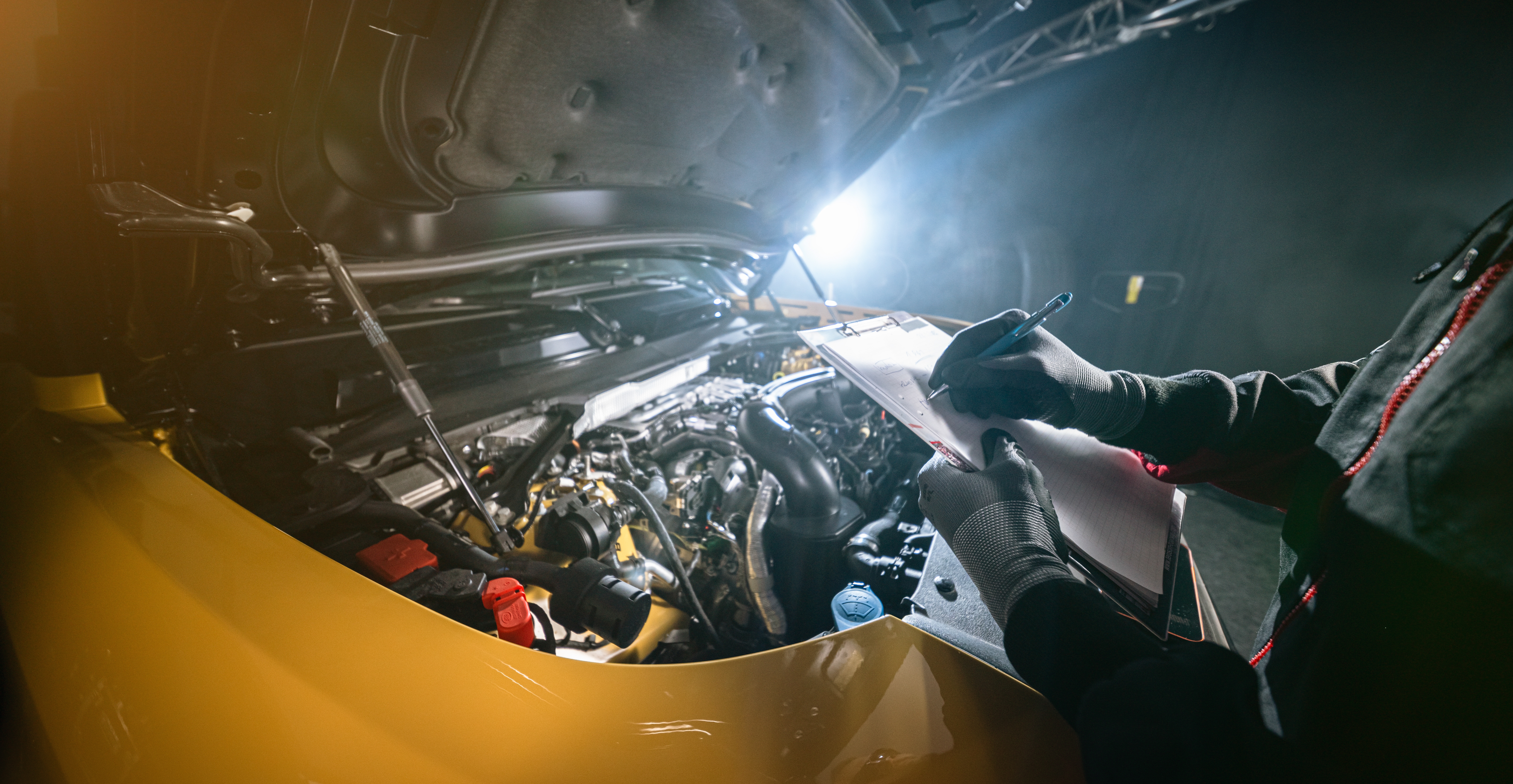 Mechanic inspecting car engine and writing notes on clipboard